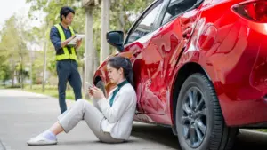 A woman leaning against her damaged car while on her phone.