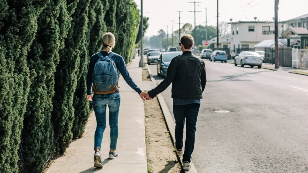 A couple holding hands and walking on a sidewalk.