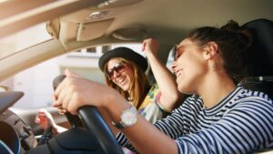 Two women singing a song inside a car.