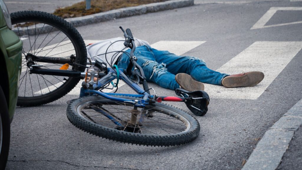 A man on laying on the road with a fallen bike right next to him.