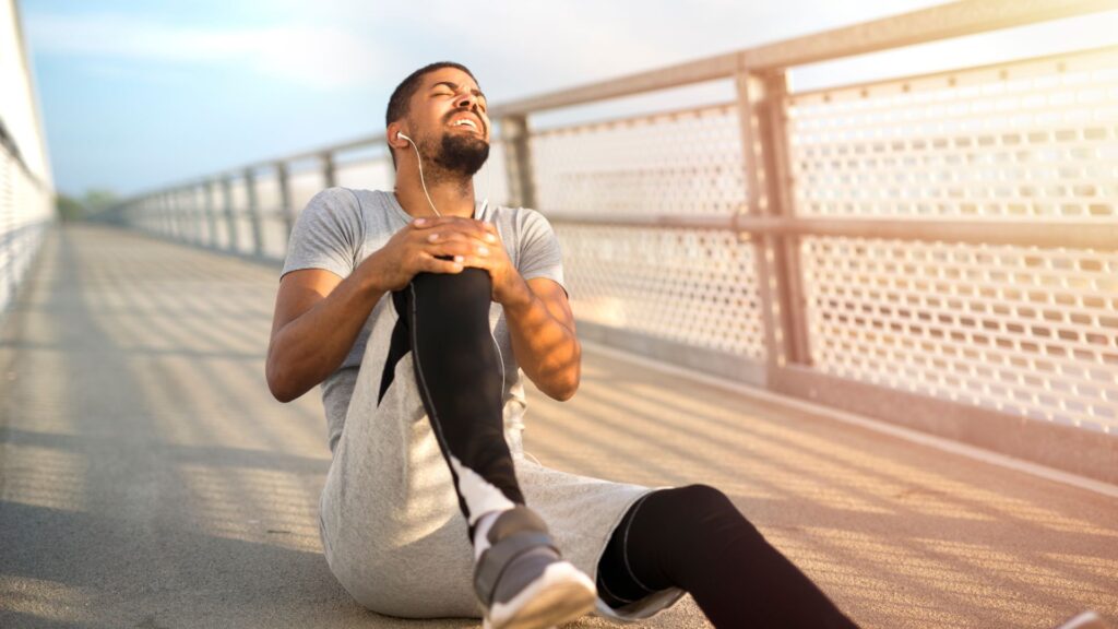 A man sitting on the ground and holding onto his knee in pain.