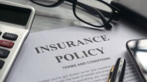 A close up of an insurance policy with a pen, calculator, and a pair of glasses around the policy.