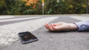 A broken cellphone and a person's hand laying in the middle of the street.