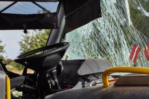 The driver's seat of a public bus where the front windshield is cracked.