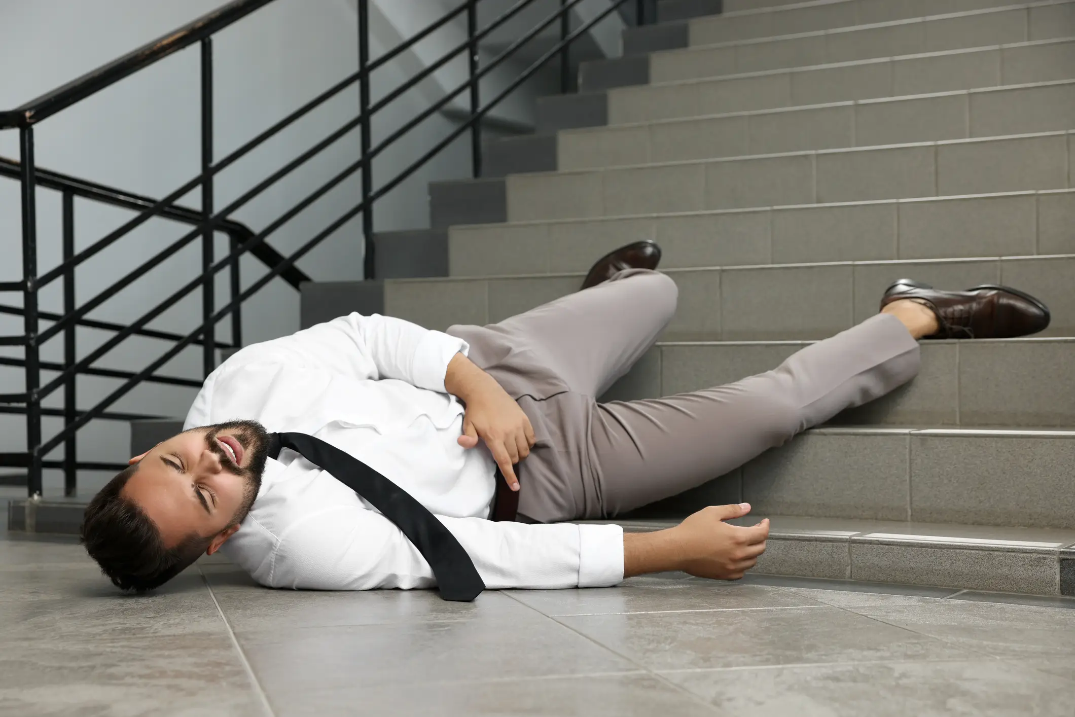 A man laying on the floor after falling from a flight of stairs.