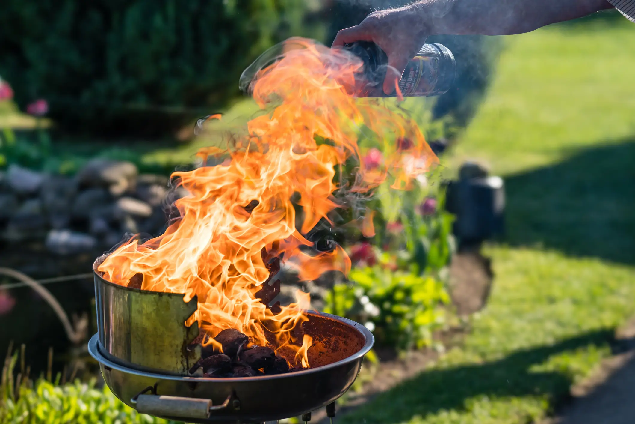 A person pouring lighter fluid on a bbq, and a big burst of flames jumps out.