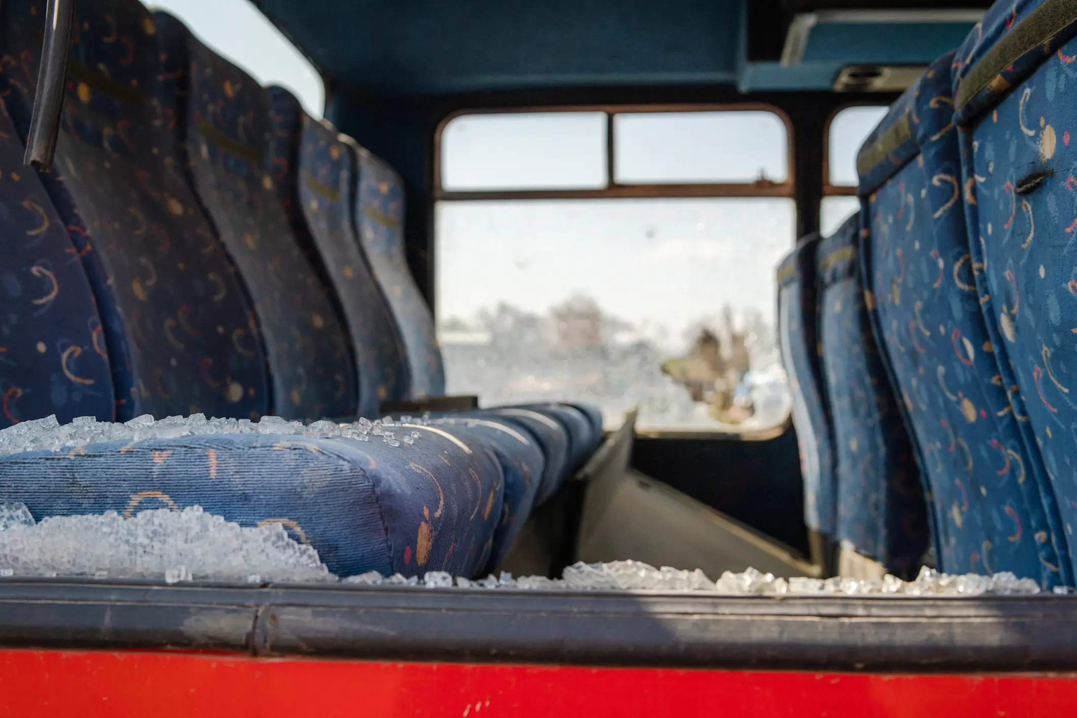 A bus with a broken window, showing broken glass all over the seats.