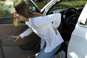 A woman getting out of her car while holding her back.