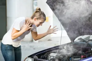 A woman stressing out with her car blowing smoke from the hood.
