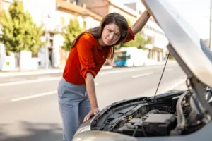 A woman opening the hood of her car looking stressed.