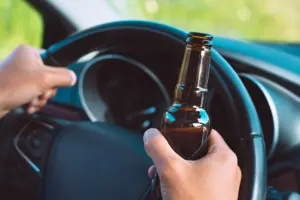 A person driving a car while holding a beer.