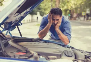 A man looking confused, stressed, and stumped at his car's engine.