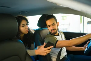 A woman showing her rideshare driver something on her phone.