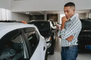A man looking at several cars at a dealership.