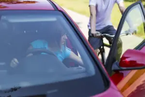 A woman opening her car door and a biker incidentally crashes into it.