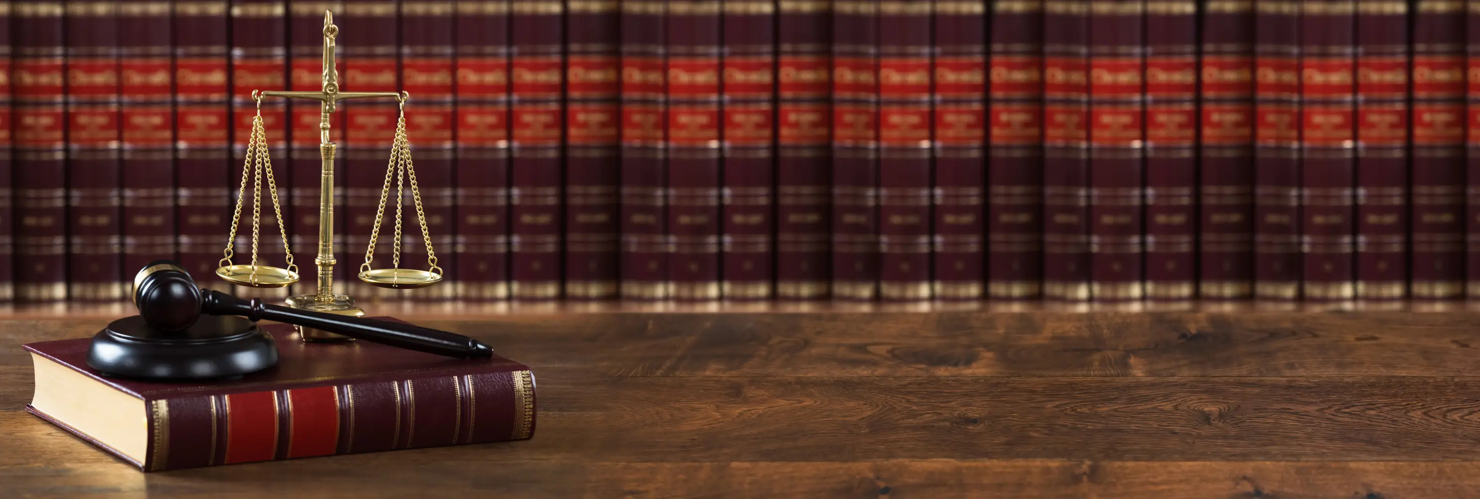 A law book and scale on a table while there is a row of books in the background. 