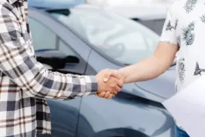 Two people shaking hands in front of a car.