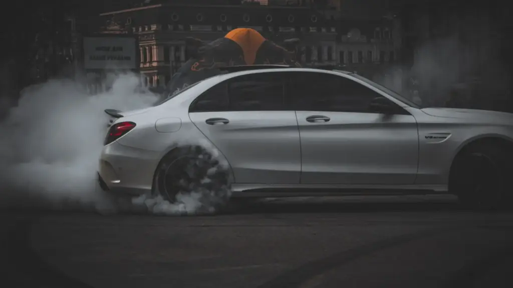 A gray car doing donuts in a middle of a street.