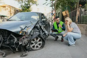 A woman and an insurance adjuster discussing damages while looking at a damaged car.