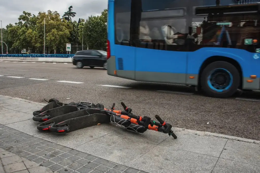 An electric scooter on its side as a bus passes by.
