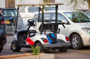 A golf kart parked in a parking lot along with other cars.