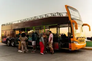 A double decker tour bus with a crowd of people waiting to get on.