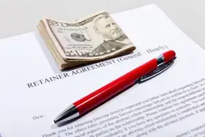 A retainer document with a red pen and a wad of bills on top.