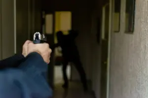A person pointing a gun at another person in a dark hallway. 