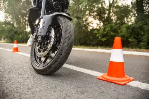 A motorcycle passing a traffic cone on the road.
