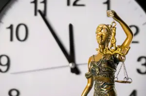 A gold statue of lady justice with a clock in the background.